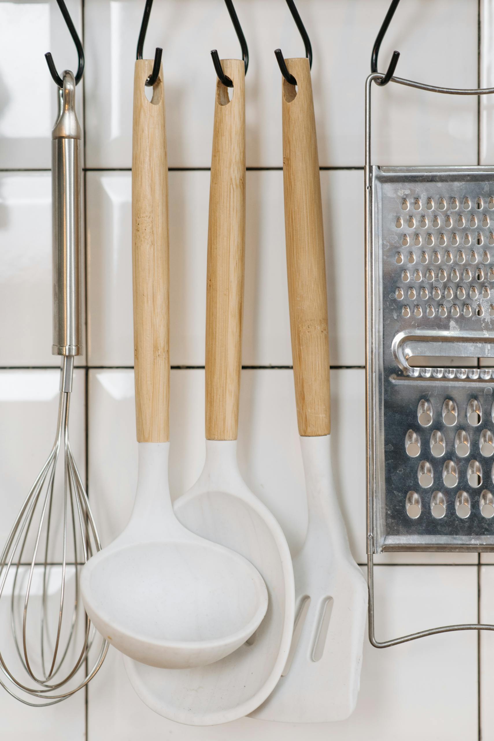 Aesthetic arrangement of kitchen utensils including a whisk, ladle, spatula, and grater on a tiled wall.