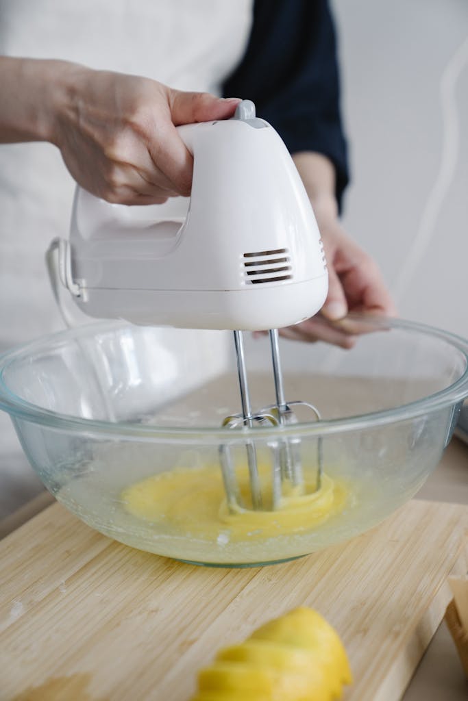Closeup of hand mixing eggs with a mixer in a glass bowl confidently Closeup of a hand holding a mixer beating eggs in a glass bowl to prepare a delicious omelette or meringue